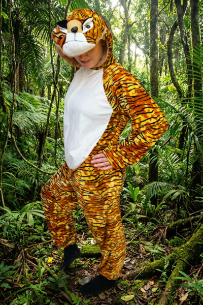 Triibulises tiigrikostüümis naine seisab tihedas rohelises metsas.