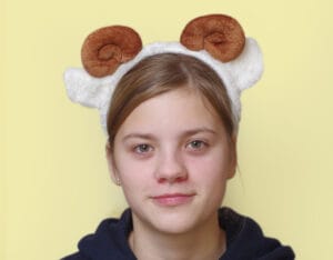 lapsel on peas pruunide keerdus sarvede ja valgete kõrvadega oina peavõru. Taust on kollane,