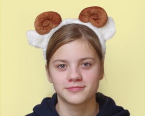 lapsel on peas pruunide keerdus sarvede ja valgete kõrvadega oina peavõru. Taust on kollane,