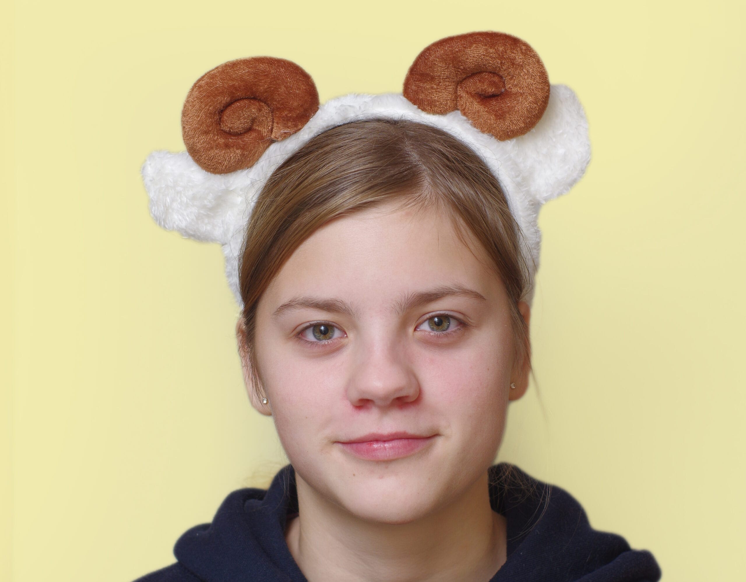 lapsel on peas pruunide keerdus sarvede ja valgete kõrvadega oina peavõru. Taust on kollane,