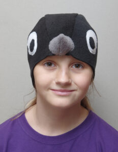 Suurte valgete silmadega ja halli nokaga musta linnu kostüümimüts lapse peas.