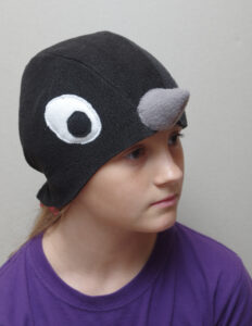 Suurte valgete silmadega ja halli nokaga musta linnu kostüümimüts lapse peas.