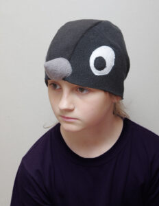 Suurte valgete silmadega ja halli nokaga musta linnu kostüümimüts lapse peas.