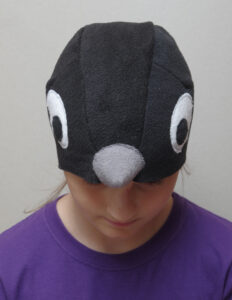 Suurte valgete silmadega ja halli nokaga musta linnu kostüümimüts lapse peas.