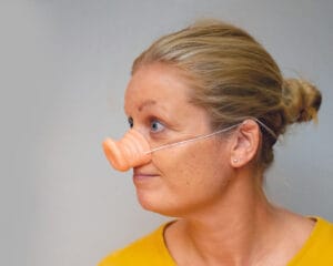 A portrait of a person with blurred face and light brown hair in a bun, wearing a yellow top. The person is wearing a decorative oversized ear accessory and a small earring. The image is captured against a neutral gray background, creating a playful and whimsical atmosphere. Portree inimesest, kelle nägu on hägustatud ja helepruunid juuksed on krunnis, seljas kollane pluus. Isik kannab dekoratiivset suurt kõrvakaunistust ja väikest kõrvarõngast. Pilt on jäädvustatud neutraalsel hallil taustal, luues mängulise ja lõbusa meeleolu.