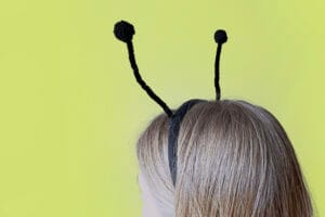 Pikkade juustega tüdrukul on peas mustade sarvedega peavõru. Tüdruk on seljaga ja taust on roheline.