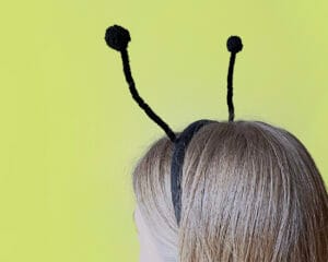 Pikkade juustega tüdrukul on peas mustade sarvedega peavõru. Tüdruk on seljaga ja taust on roheline.