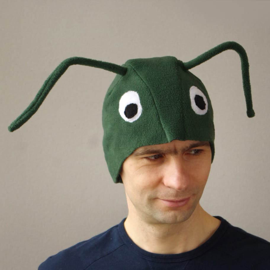 Tumeroheline fliisist putukakostüümi müts, millel on suured silmad ja tundlad. Müts on peas täiskasvanud mehel."