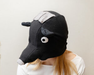 Handmade black bear costume hat made of fleece, featuring a unique white fringe on top and a white nose.