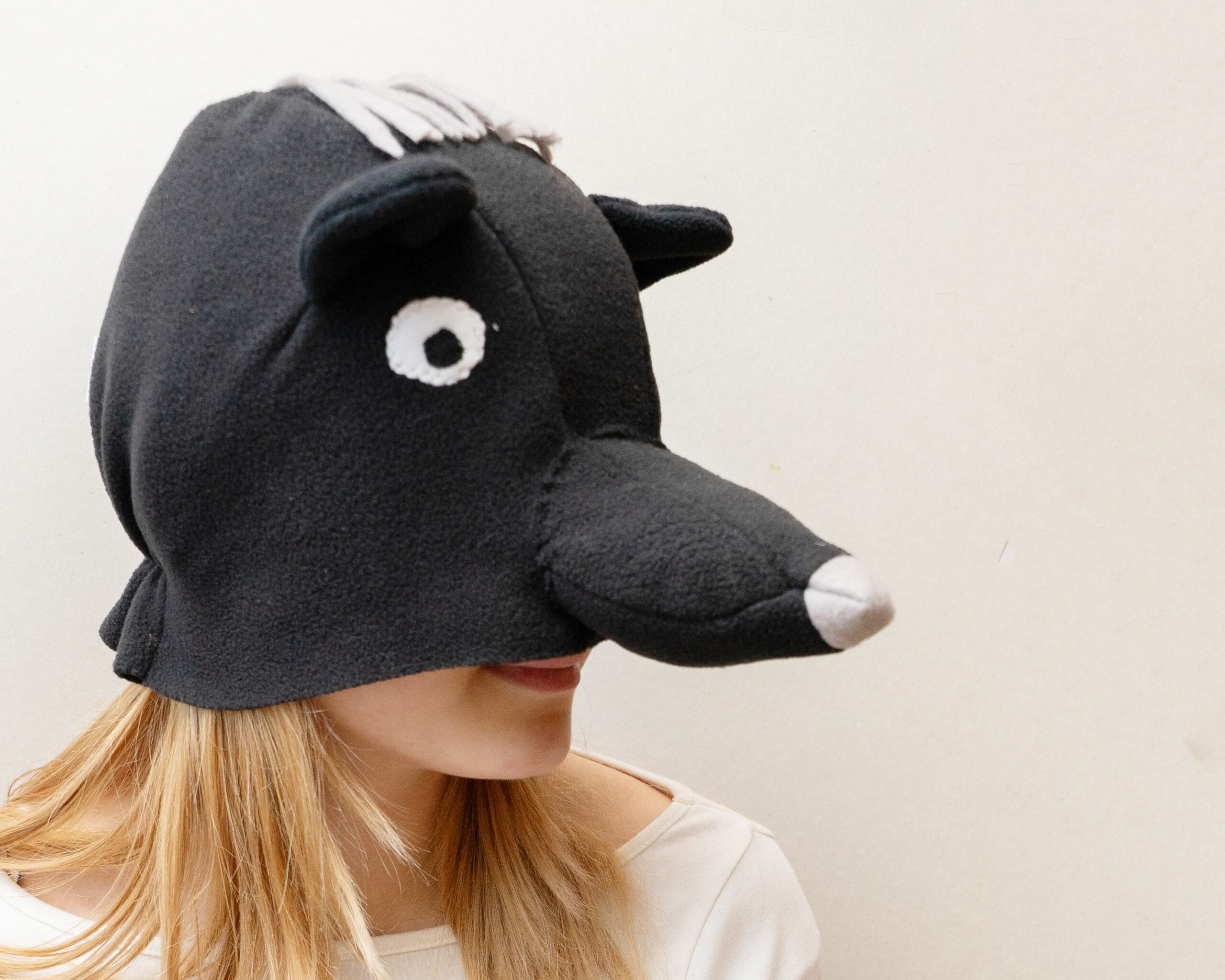 Handmade black bear costume hat made of fleece, featuring a unique white fringe on top and a white nose.