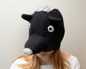 Handmade black bear costume hat made of fleece, featuring a unique white fringe on top and a white nose.