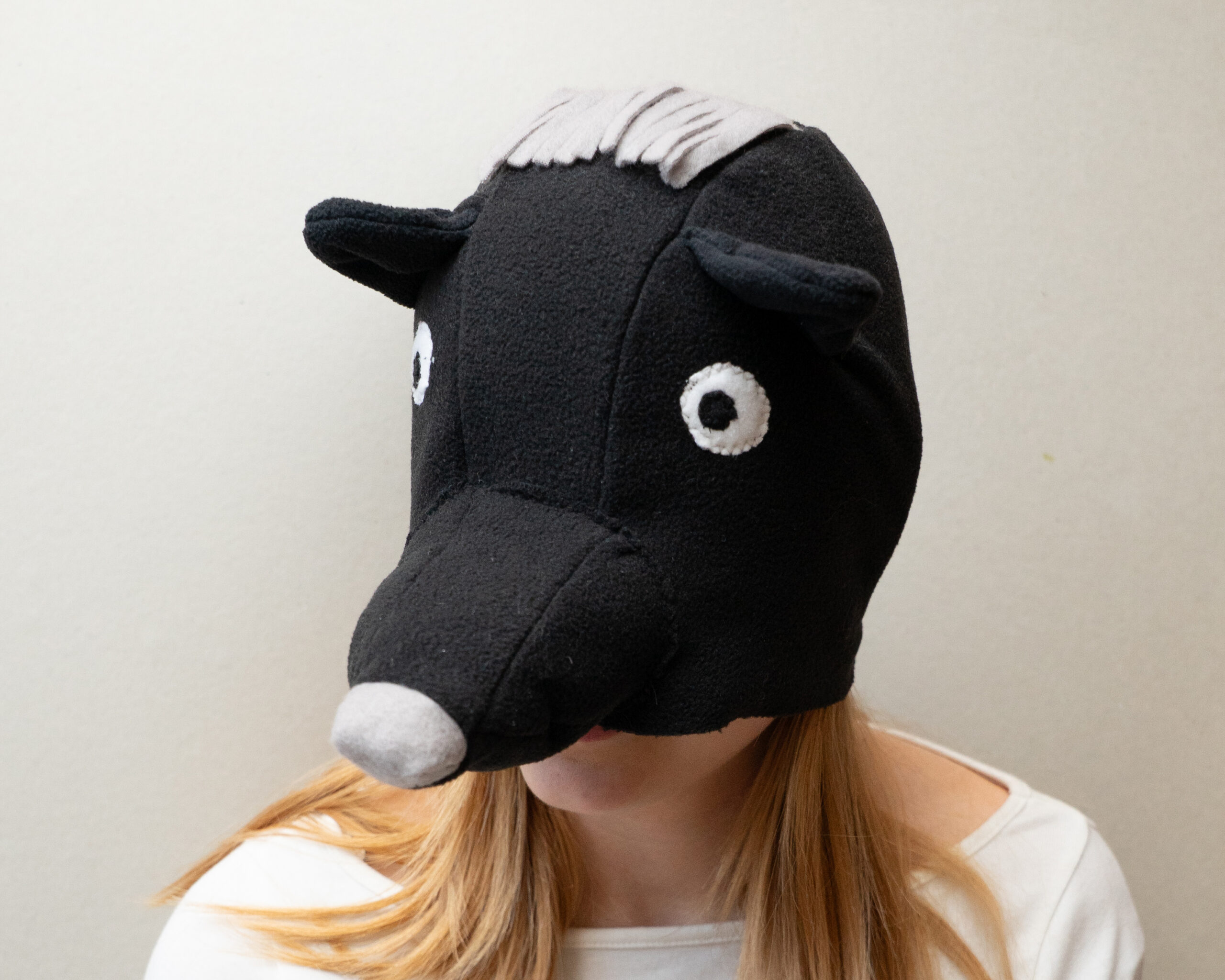 Handmade black bear costume hat made of fleece, featuring a unique white fringe on top and a white nose.