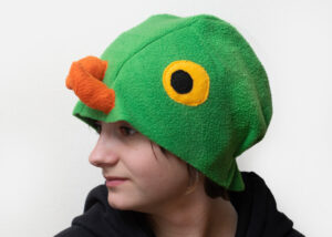 Handmade vibrant green fleece bird hat for adults with an orange beak and large yellow-black eyes.