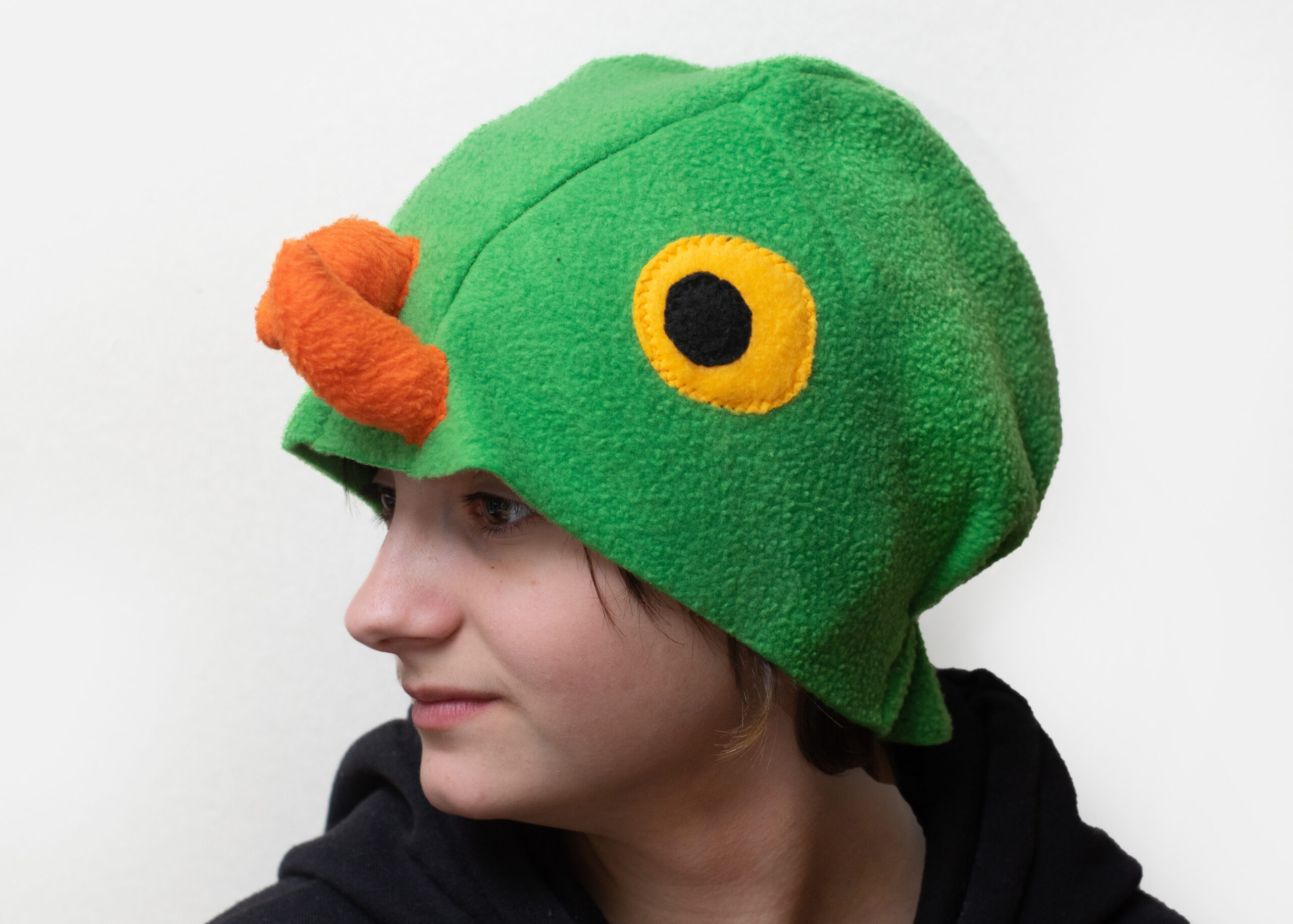 Handmade vibrant green fleece bird hat for adults with an orange beak and large yellow-black eyes.