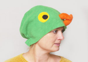 Handmade vibrant green fleece bird hat for adults with an orange beak and large yellow-black eyes.