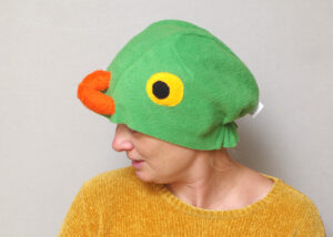 Handmade vibrant green fleece bird hat for adults with an orange beak and large yellow-black eyes.