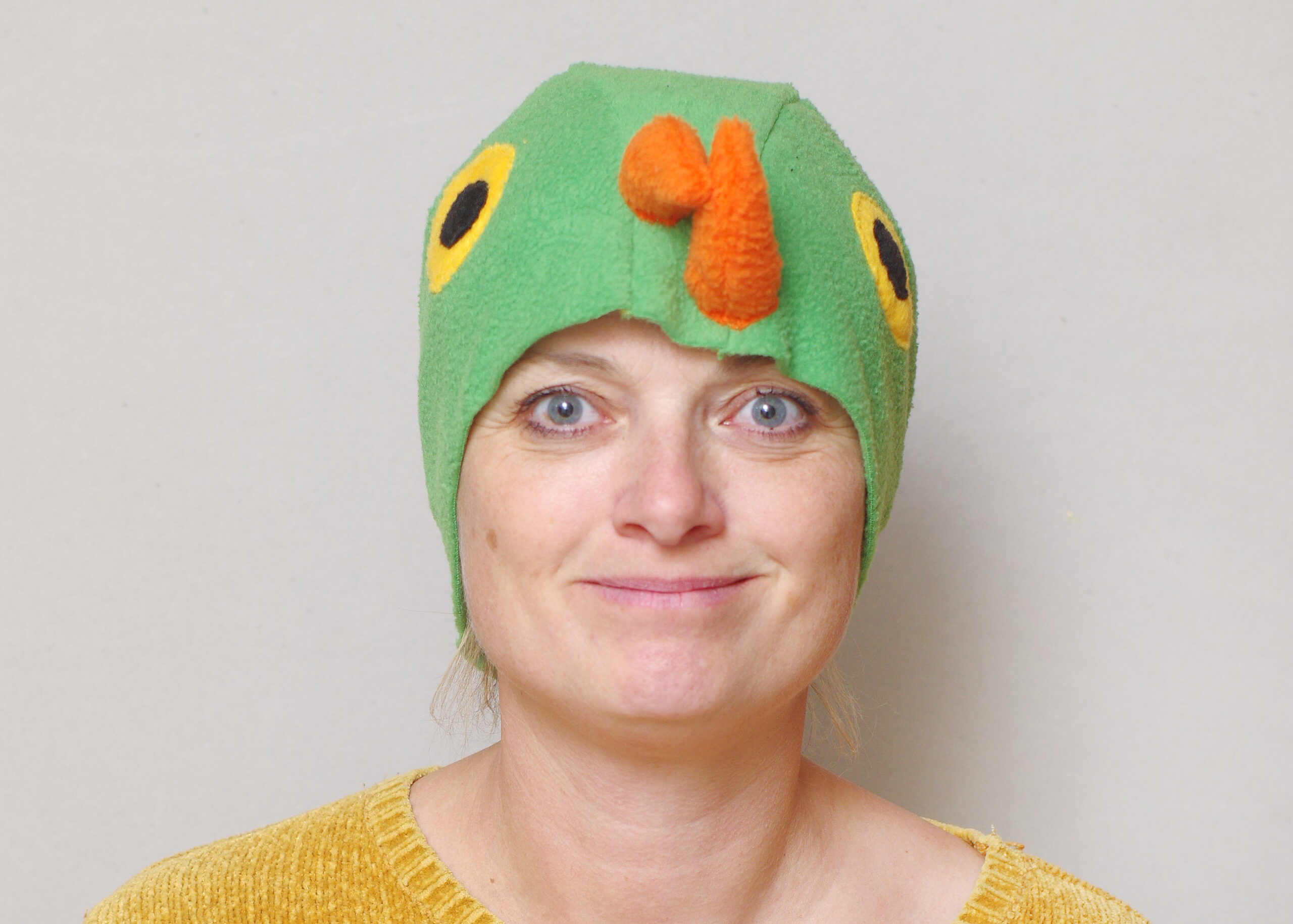Handmade vibrant green fleece bird hat for adults with an orange beak and large yellow-black eyes.