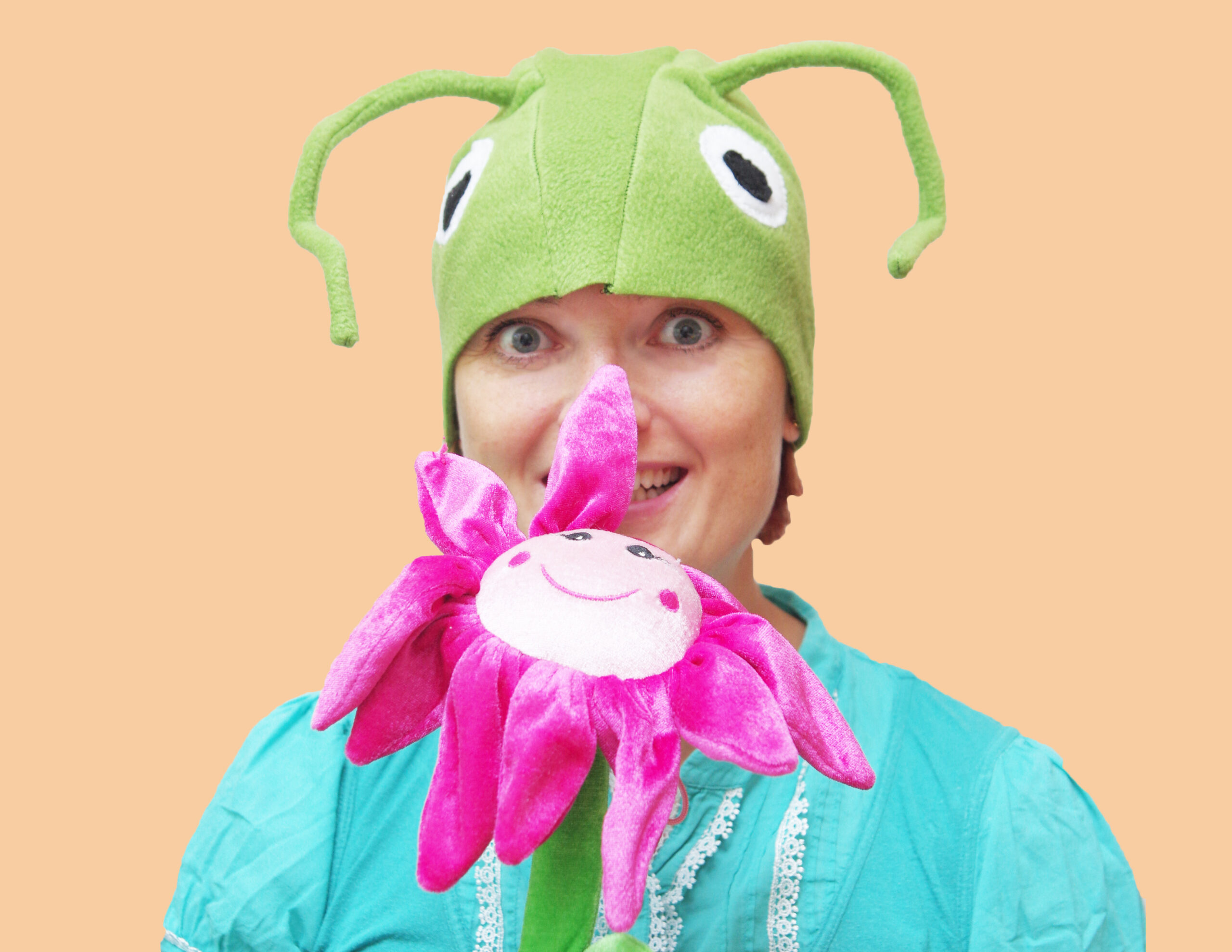 Naine kannab suurte valgete silmade ja pikkade tundlatega helerohelise rohutirtsu kostüümi- Käes on suur neoonroosa naerunäoga lill.